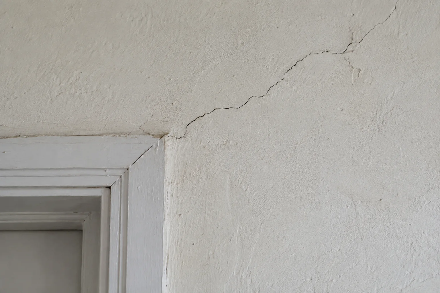 Fissure fine en biais partant de l'angle d'une porte dans un enduit ancien (illustration générée par IA)